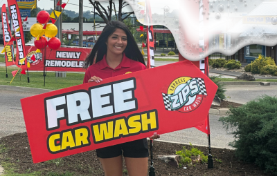 Woman holding "Free Car Wash ZIPS Car Wash" sign, smiling in front of newly remodeled ZIPS Car Wash location