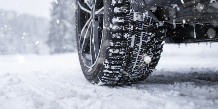 Close-up of a car tire covered in snow on a snowy road.